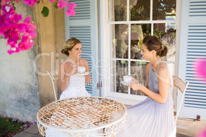 Bride and bridesmaid having coffee in yard