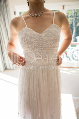 Midsection of woman in wedding dress standing at home