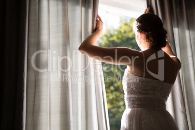 Rear view of bride in wedding dress looking through window at home