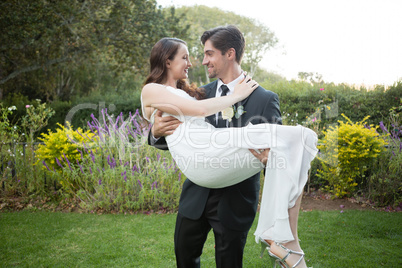 Bridegroom carrying bride while walking in park