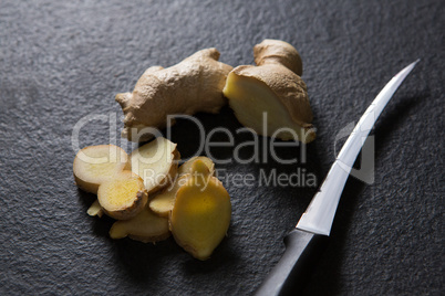 Sliced ginger with knife on black background