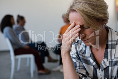 Woman with head in hand while friends discussing in background