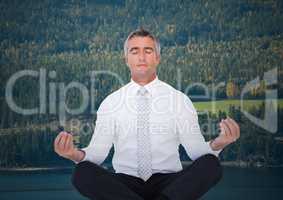 Business man meditating against trees and river