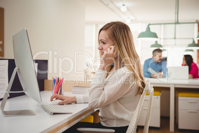 Female executive talking on mobile phone while working on computer