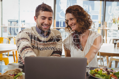 Smiling man with woman using laptop in cafe