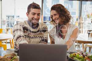 Smiling man with woman using laptop in cafe