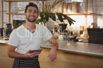 Portrait of waiter with tablet by counter at cafe