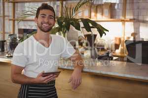 Portrait of waiter with tablet by counter at cafe