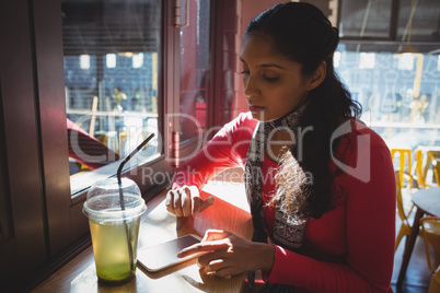 Woman with drink using phone in cafe