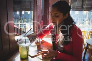 Woman with drink using phone in cafe