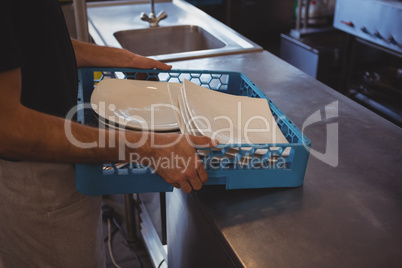 Mid section of waiter arranging plates in crate