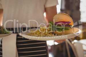 Mid section of waiter holding plate with burger and French fries