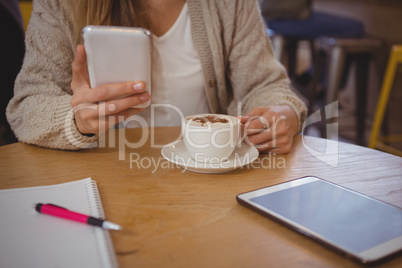 Mid section of woman with coffee using phone