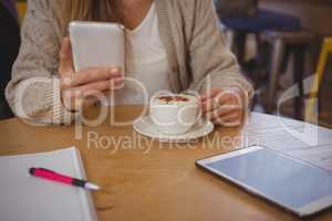 Mid section of woman with coffee using phone