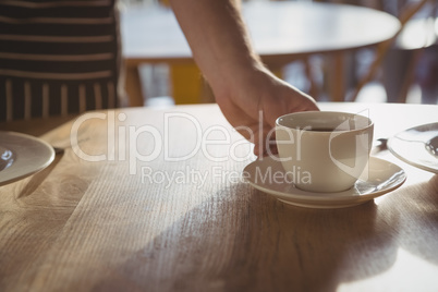 Cropped hand of waiter serving coffee on table