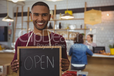 Portrait of owner with open sign in cafe