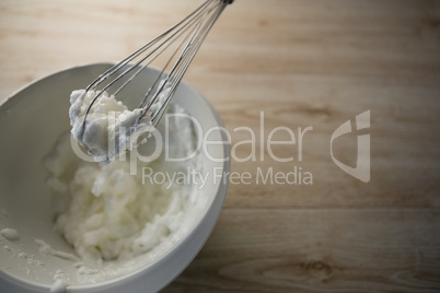 High angle view of wire whisk with whipped cream on bowl