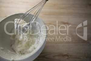 High angle view of wire whisk with whipped cream on bowl