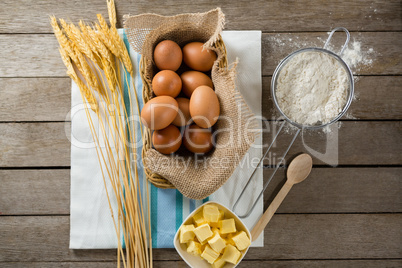 Eggs in wicker basket with wheat, cheese, and flour on wooden table