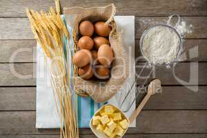 Eggs in wicker basket with wheat, cheese, and flour on wooden table