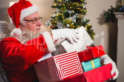 Santa claus sitting with stack of gift boxes in living room