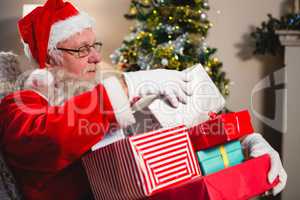 Santa claus sitting with stack of gift boxes in living room