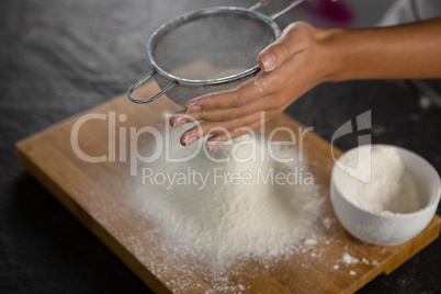 Woman sieving flour from the bowl on the wooden board