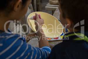 Female potter assisting her son in painting a bowl