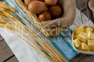 Eggs in wicker basket with wheat and cheese on wooden table