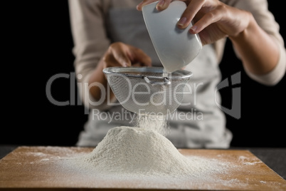 Woman sieving flour from the bowl on the wooden board
