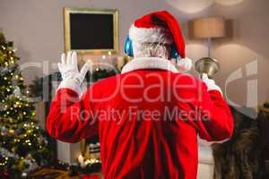 Santa claus listening to music on headphones at home during christmas time