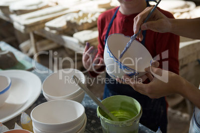 Mid section of female potter and boy painting bowl