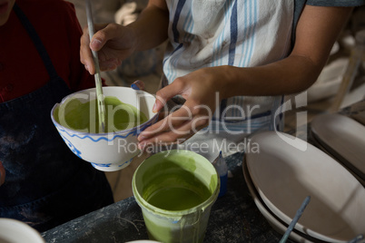 Mid section of female potter and boy painting bowl