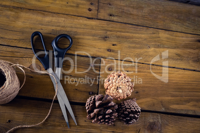 Pine cone, scissor and thread on wooden table