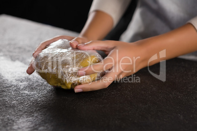 Woman holding dough wrapped with plastic in her hand
