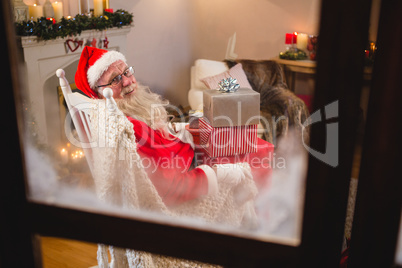 Santa claus sitting with stack of gift boxes in living room during christmas time