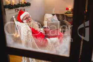 Santa claus sitting with stack of gift boxes in living room during christmas time