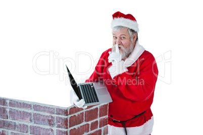 Santa claus with finger on lips while using laptop against white background