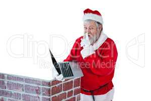 Santa claus with finger on lips while using laptop against white background