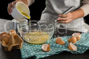 Woman adding oil into beaten eggs in a bowl