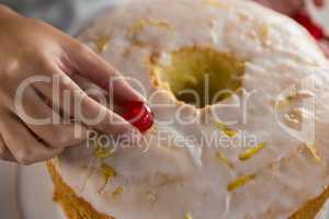 Woman toping a fresh baked cake with cherry