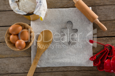 Butter paper, flour, rolling pin cookie cutter and eggs kept over a wooden table