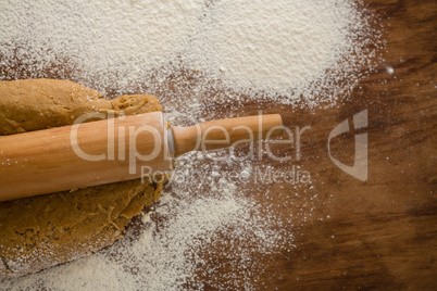 Flattening dough with rolling pin with sprinkled over flour on a wooden table