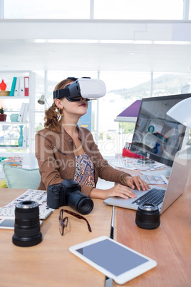 Female executive working on laptop while using virtual reality headset