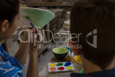 Female potter assisting her son in painting a bowl