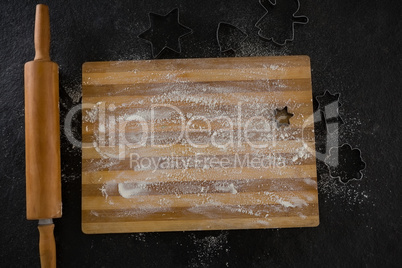 Flour on chopping board with various cookie cutters and rolling pin