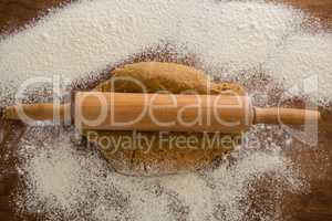Flattening dough with rolling pin with sprinkled over flour on a wooden table