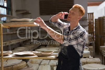 Male potter taking on mobile phone while working