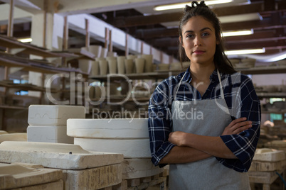 Female potter standing with arms crossed in pottery workshop