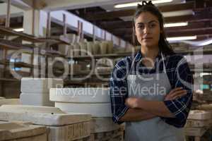 Female potter standing with arms crossed in pottery workshop